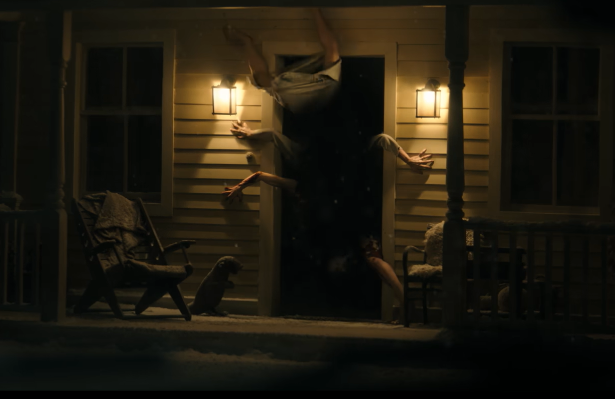 Monstro com diversas pernas e braços pendurado em uma porta no filme Resident Evil (2026).